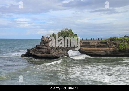 Wellen kommen an einer Felsklippe unterhalb des Batu Bolong Tempels an. Tanah Lot Tempel. Riesiges Loch in Felsklippe unterhalb Pura Batu Bolong Tempel. Hindu-Tempel auf der Be Stockfoto