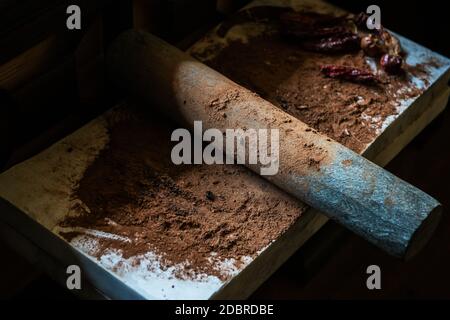 Mahlen von Kakaobohnen mit Chili-Paprika, um Schokolade von Stein Rolling Pin auf Steinoberfläche zu machen. Handgemachte Schokolade. Stockfoto