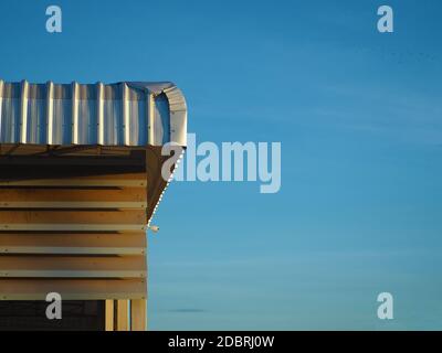 Das Blechdach der Fabrik erhält Sonnenlicht von der Morgensonne. Auf einem Hintergrund, der blauer Himmel ist. Industriekonzept. Stockfoto