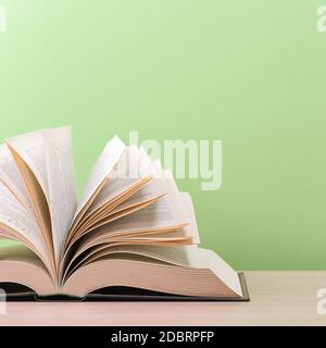 Ein großes, dickes Hardcover-Buch liegt auf einem Tisch aus hellem Holz. Das Buch ist geöffnet, die Blätter der Seite werden ausgefächert, und die Rückseite ist grün Stockfoto