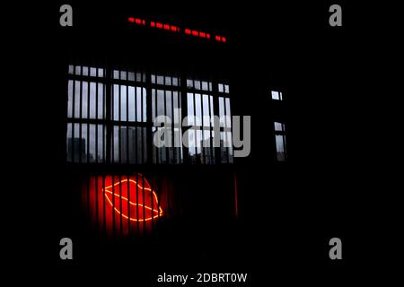 Neonlicht-Lippen hinter Bars unter einem schmutzigen Fenster mit Blick auf die trübe düstere Stadtlandschaft Stockfoto