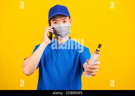 Asiatische junge gut aussehende Lieferung Mann trägt Gesichtsmaske schützende halten Alkohol Desinfektionsgel und Anruf an Kunden von Handy Studio Schuss isolieren Stockfoto