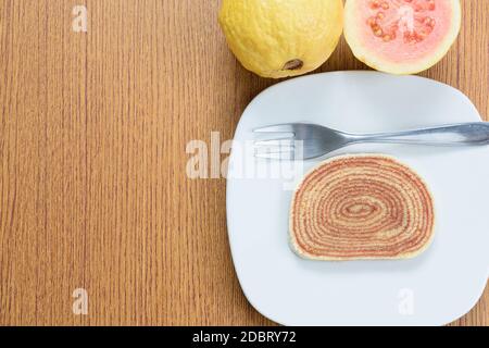 Ein Stück Kuchen (bolo de rolo) neben Guavas und einer Gabel. Stockfoto