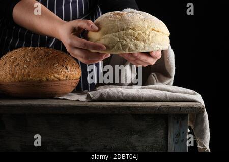 Weibliche Hände halten Runde gebackenen Weizen Mehl Brot über Holz- Tabelle, in der Nähe Stockfoto