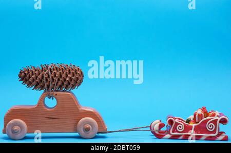 Holzspielzeug Auto trägt auf der Oberseite ein Pine Cone auf einem blauen Hintergrund, Weihnachten Hintergrund Stockfoto