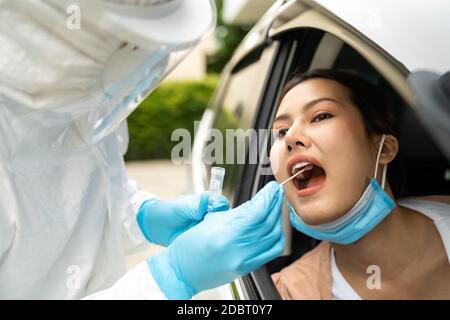 Portrait der asiatischen Frau Drive thru Coronavirus covid-19 Test durch medizinisches Personal mit PSA Anzug durch Rachenabstrich. Neue normale Gesundheitsversorgung Drive-Thru-Service A Stockfoto