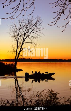 Fischer in einem Boot durch den Sonnenaufgang über einem Silhouetten Ruhiger Indian Lake Stockfoto
