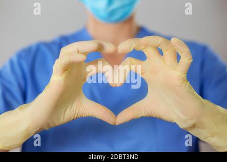 Studio-Nahaufnahme einer Krankenschwester in blauen Peelings, die mit den Fingern vor ihr eine Herzform bilden. Medizinische Arbeiter, die Liebe und Solidarität zeigen. Stockfoto