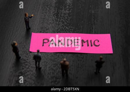 Strategie-Meeting mit Miniaturfiguren als Geschäftsleute, die um Post-it-Notiz mit Pandemic Botschaft, minimalistische abstrakte Konzept ima Stockfoto