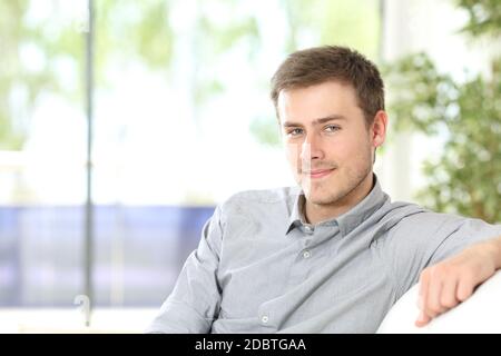 Porträt eines jungen Mannes, der die Kamera betrachtet, die zu Hause auf dem Sofa sitzt Stockfoto