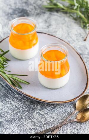 Hausgemachte Panna Cotta mit Scheiben von Pfirsich und Pfirsich Gelee in Glasgefäßen auf einem grauen Beton Hintergrund. Stockfoto