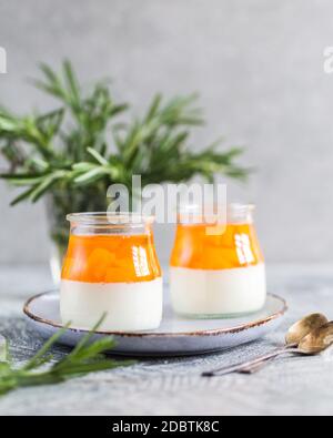 Hausgemachte Panna Cotta mit Scheiben von Pfirsich und Pfirsich Gelee in Glasgefäßen auf einem grauen Beton Hintergrund. Stockfoto