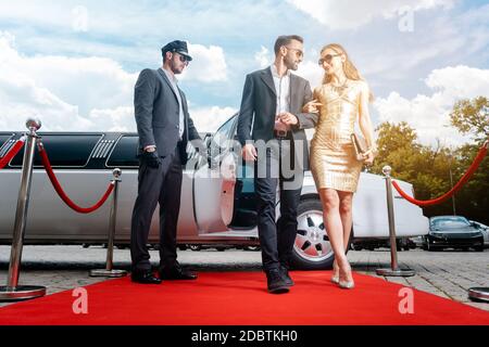Ein Paar, das mit einer Limousine anreist und den roten Teppich läuft, öffnet die Autotür Stockfoto