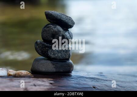 Kleiner Stapel von Kieselsteinen oder Steinen in einem Bach sorgfältig aufeinander ausgeglichen mit plätschernden sonnigem Wasser fließt vorbei Stockfoto