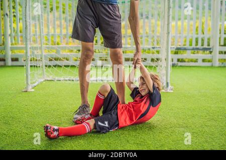 Kleiner niedlicher Junge in roter Fußballuniform und sein Trainer oder Vater spielt Fußball, Fußball auf dem Feld, im Freien. Aktives Kind macht Sport mit Stockfoto