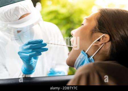 Portrait der asiatischen Frau Drive thru Coronavirus covid-19 Test durch medizinisches Personal mit PSA Anzug durch Rachenabstrich. Neue normale Gesundheitsversorgung Drive-Thru-Service A Stockfoto