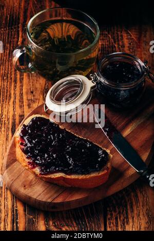 Toast mit Beeren Marmelade auf Schneidebrett und Tasse grüner Tee Stockfoto