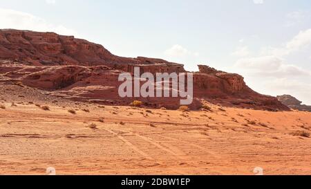 Felsige Massive auf roter Sandwüste, heller Wolkenhimmel im Hintergrund - typische Landschaft im Wadi Rum, Jordanien. Stockfoto