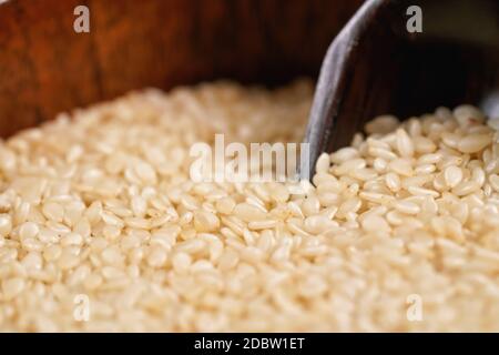 Weißer Sesam - Sesamum indicum - Samen in kleiner Holzschale mit Schaufel - Nahaufnahme Makro Detail. Stockfoto