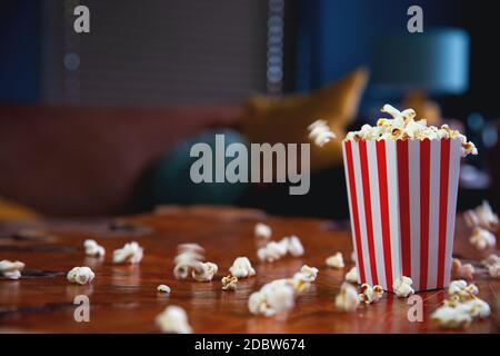 Popcorn fliegen aus Karton. Rot-weiß gestreifter Popcorn-Eimer mit fliegendem Popcorn im Wohnzimmer, Film- oder Kinokonzept Food oder Snac Stockfoto