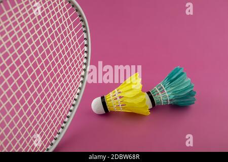 Badmintonschläger und bunte Federhähne in Grün und Gelb auf rosa Hintergrund Stockfoto