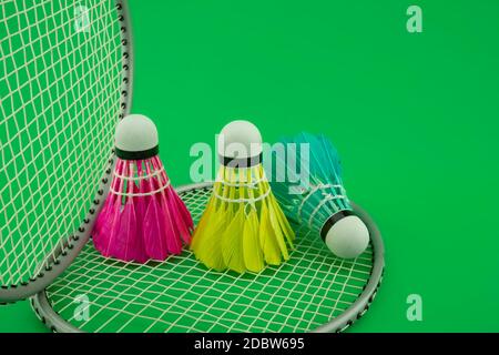 Badminton Schläger und bunt gefiederte Bälle in Blau, Gelb und Rosa auf grünem Hintergrund in der Nähe zu sehen. Stockfoto