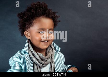 Portrait eines netten kleinen afroamerikanischen Jungen in stylischen Kleidern, der auf dunklem Hintergrund im Studio posiert. Babymodell. Stockfoto