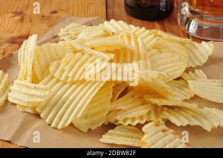 Wellige Kartoffelchips auf braunem Papier mit einer Tasse Bier im Hintergrund Stockfoto