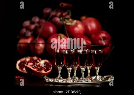 Still-Leben auf einem dunklen Hintergrund. Weingläser (Liquor), Früchte und Beeren (Äpfel, Granatäpfel und Trauben) in den Korb. Stockfoto