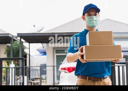 Asiatische Lieferung Express Kurier junger Mann geben Boxen an Frau Kunde trägt er schützende Gesichtsmaske vor Hause, unter Sperrstunde Quarantäne Pandemi Stockfoto