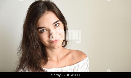 Porträt der jungen 25 Jahre Brünette russische Frau mit langen Haaren. In weiß offene Schulter oben und Blick in die Kamera auf hellgrauem Hintergrund. Stockfoto