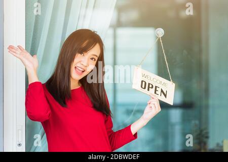 Asiatische junge Frau froh und lächelnd sie bemerken Schild Holzbrett Label 'WILLKOMMEN OFFEN' hängen durch Glastür Front Shop, Business Drehen offen nach Stockfoto