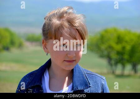 Porträt von 10 Jahre alten russischen lächelnden blonden Mädchen auf einem Hintergrund von grünen Feld. Nettes Gesicht, wegschauen