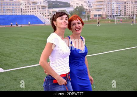 Zwei glückliche junge Schwestern lachen beim Fußballtraining am Sommerabend aufrichtig über das Fußballfeld. Stockfoto