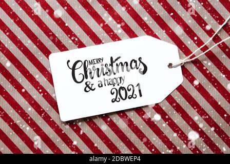Label mit englischer Kalligraphie Frohe Weihnachten und EIN glückliches 2021. Rotes Geschenkpapier Als Hintergrund Mit Schneeflocken Stockfoto
