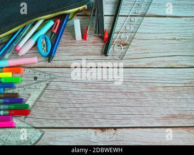 Die Draufsicht auf Schreibwaren in Schultaschen und Bleistiften auf einem Holztebelhintergrund angeordnet. Stockfoto