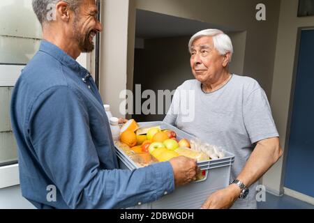 Hilfe Beim Einkaufen Von Lebensmitteln Für Älteren, Der Vor Der Tür Steht Stockfoto