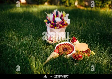 Teeparty, Süßigkeiten, frischer Berrie und Blumen auf dem Gras, niemand. Romantisches Bankett im Freien. Hochzeitsfeier auf Sommerwiese Stockfoto