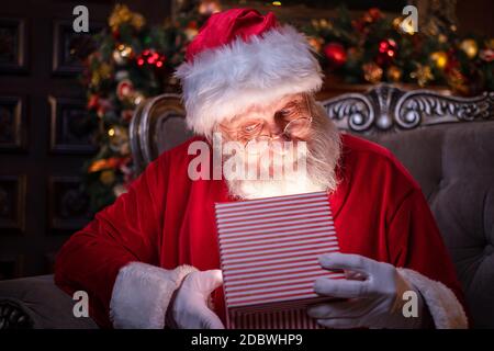 Weihnachtsmann Eröffnung Weihnachtsgeschenk. Erfüllung von Wünschen. Santa sitzt zu Hause in der Nähe von Weihnachtsbaum Stockfoto