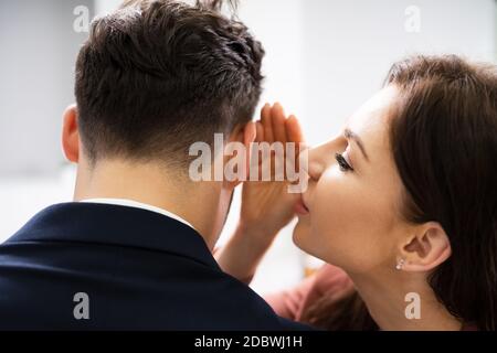 Frau flüstert Klatsch in Friends Ohr am Arbeitsplatz im Büro Stockfoto