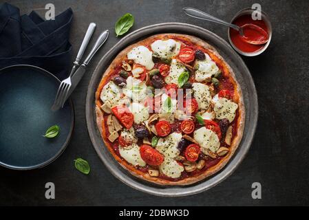 Frische Pizza mit Tomatensauce, Pilze, schwarze Oliven, Mozzarella-Käse, Schinken auf dunklem Tisch Nahaufnahme Stockfoto