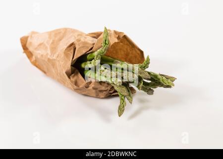 Selektiver Fokus einer Handvoll wilder Spargel in braunen Papiertüten auf einem unscharfen hellen Hintergrund eingewickelt. Frisches und veganes Lebensmittelkonzept. Stockfoto