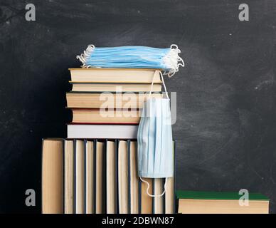 Stapel von verschiedenen Büchern und Einweg-medizinische Masken auf dem Hintergrund einer leeren schwarzen Kreidetafel, Konzept des Besuchs Bibliotheken in persönlichen Schutz Stockfoto