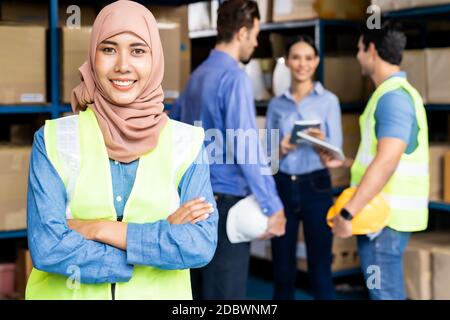 Portrait of Islam muslimische Lagerarbeiterin kreuzte den Arm mit ihren Kollegen, die sich im Lager-Distributionszentrum treffen. Für Geschäftsreisende wa Stockfoto