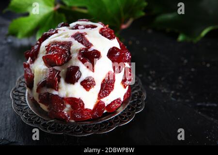 Weicher Dessertkäse mit Preiselbeeren und Traubenblättern auf schwarzem Hintergrund. Süßer Käse zum Frühstück. Köstliches Dessert. Speicherplatz kopieren. Stockfoto