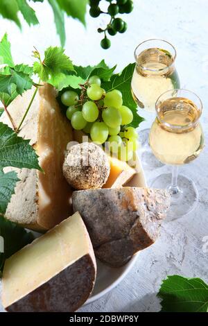 Verschiedene Hartkäse mit zwei Gläsern Wein und grünen Trauben auf hellem Hintergrund. Vertikales Foto. Draufsicht. Stockfoto