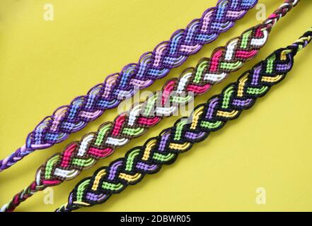 Selektiver Fokus der mehrfarbigen gewebten DIY Freundschaft Armbänder Pigtail handgefertigt Aus Stickerei heller Faden mit Knoten auf gelbem Hintergrund Stockfoto