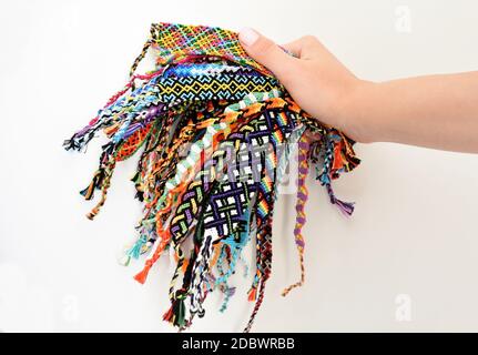 Weibliche Hand hält viele gewebte mehrfarbige DIY Freundschaft Armbänder handgefertigt von Stickerei Thread mit Knoten auf weißem Hintergrund. Stockfoto