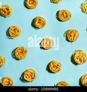 Pasta Art. Tagliatelle auf blauem pastellfarbenem Hintergrund in hartem Licht. Kreatives Layout mit Nudelnudeln, Draufsicht oder Flat Lay. Quadratisches Erntegut. Kreatives Design Stockfoto