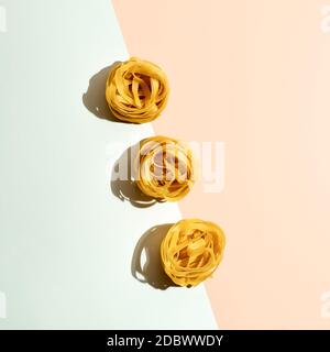 Pasta Art. Tagliatelle auf blau und creme duotone Pastell Hintergrund in hartem Licht. Kreatives Layout mit Nudelnudeln, Draufsicht oder Flat Lay. Kreative d Stockfoto